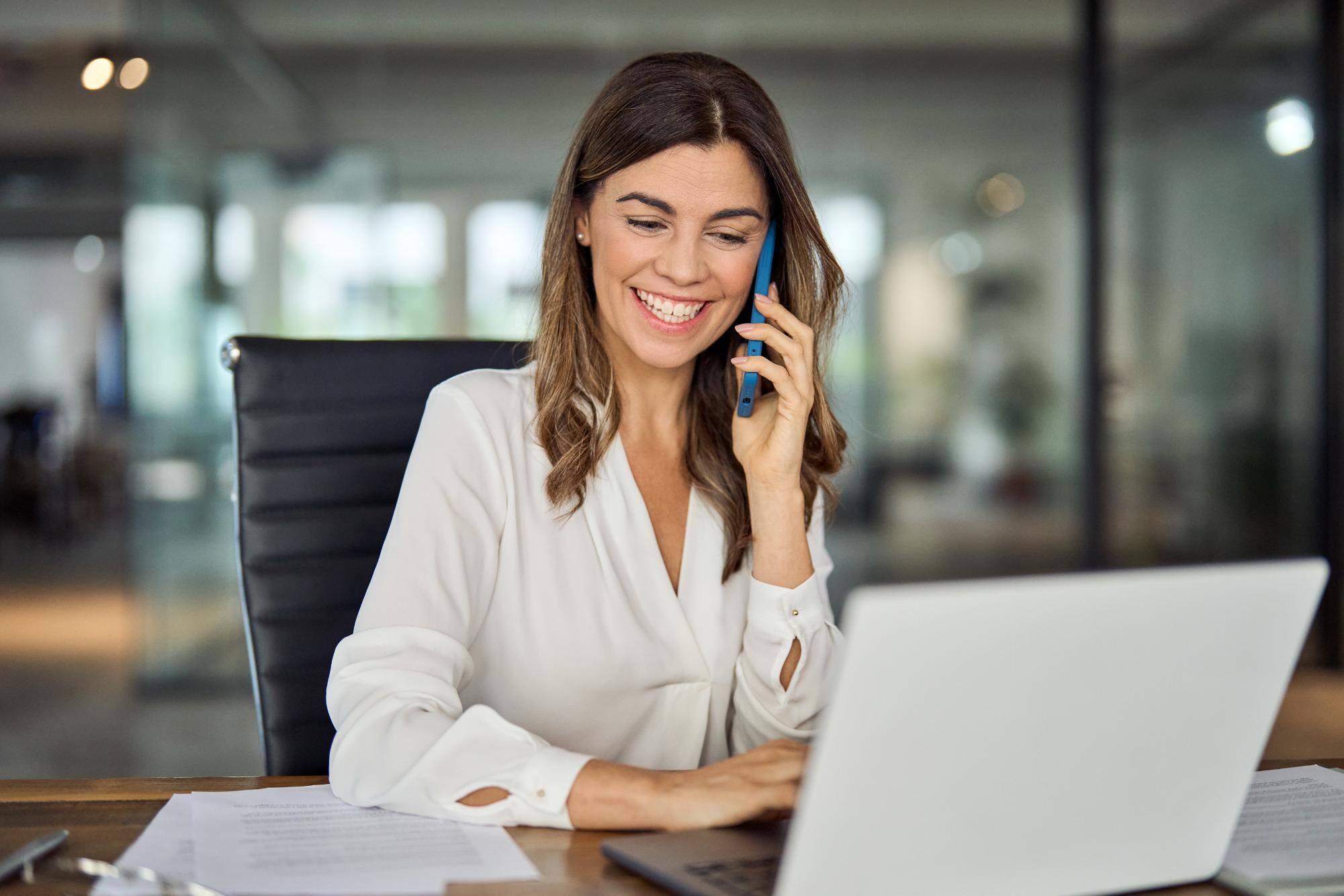 Business lady talking on the phone while sitting at a desk working on computer